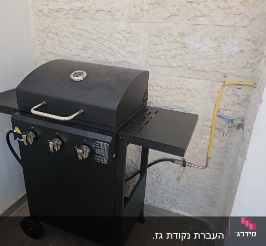 גריל גז שחור עם שלושה כפתורים וצינור גז צהוב